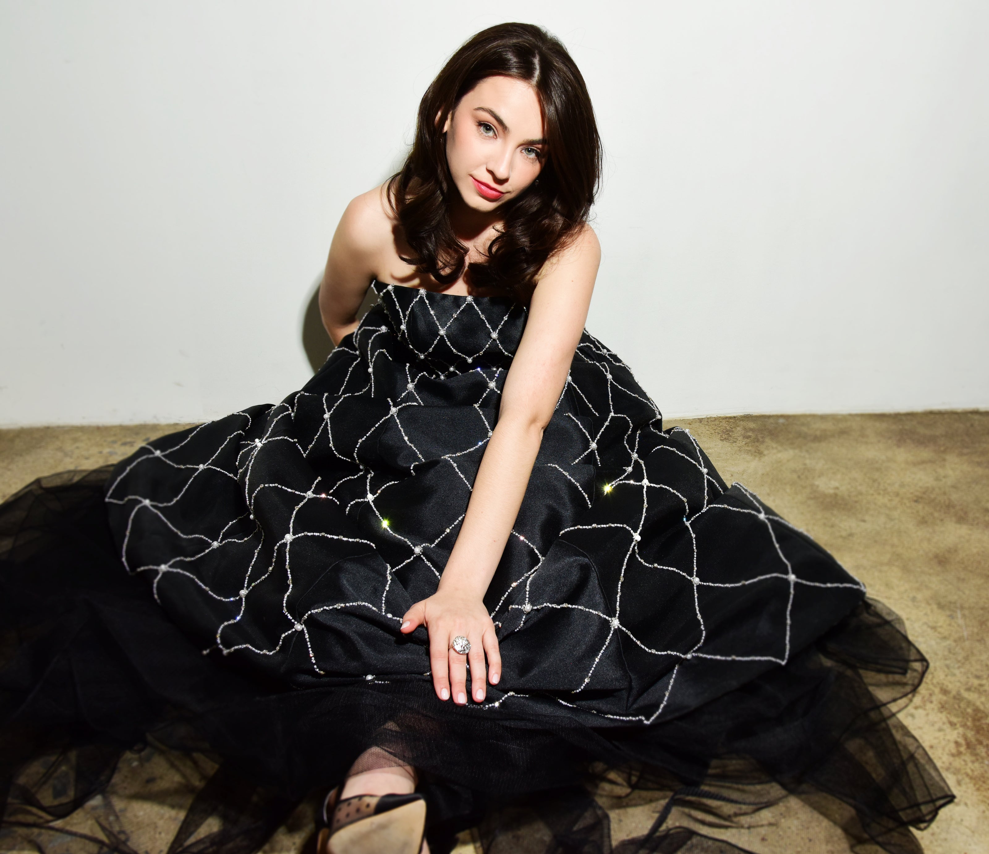Woman in a black dress with white patterns sitting on a beige carpet.