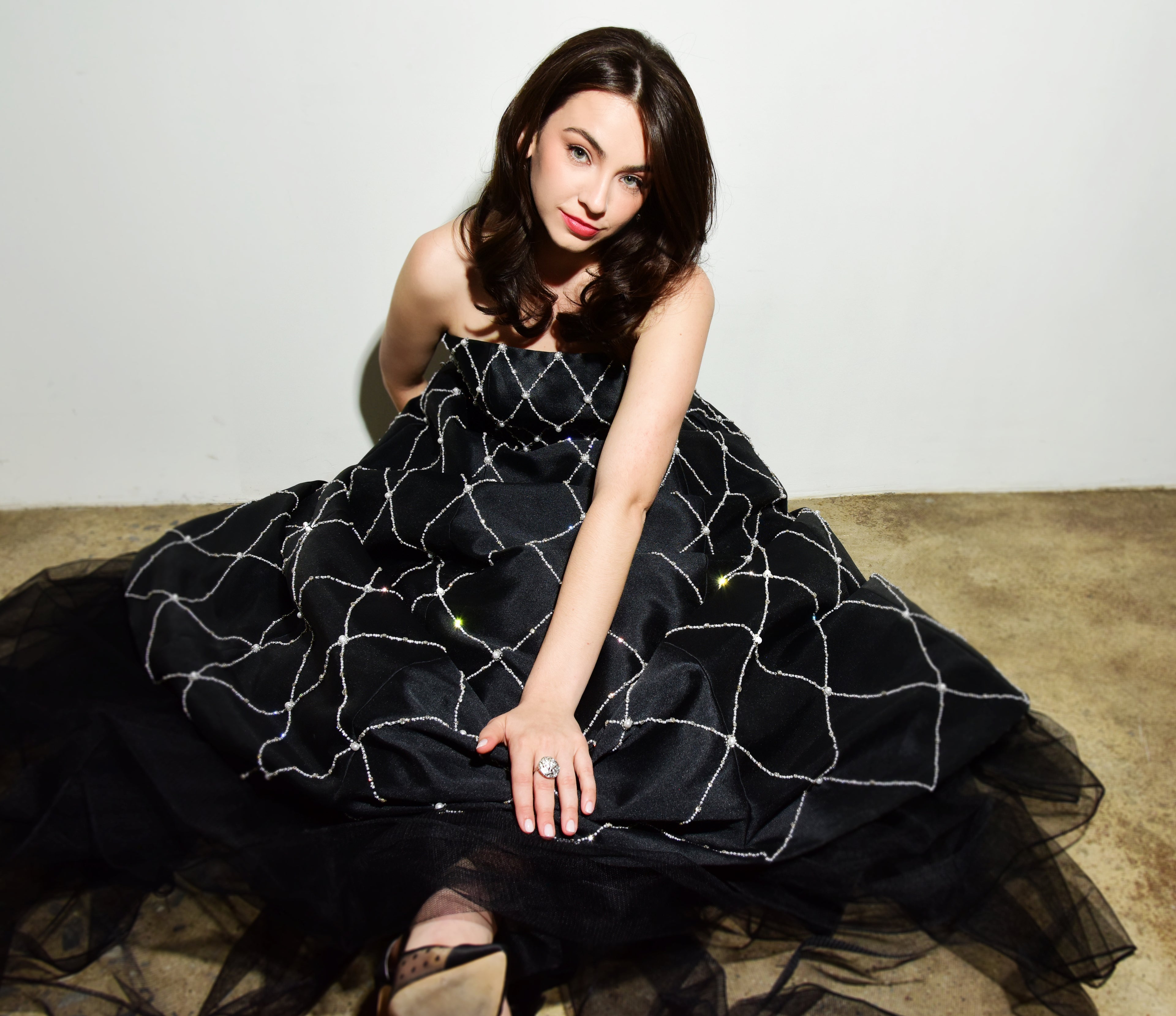 Woman in a black dress with white patterns sitting on a beige carpet.